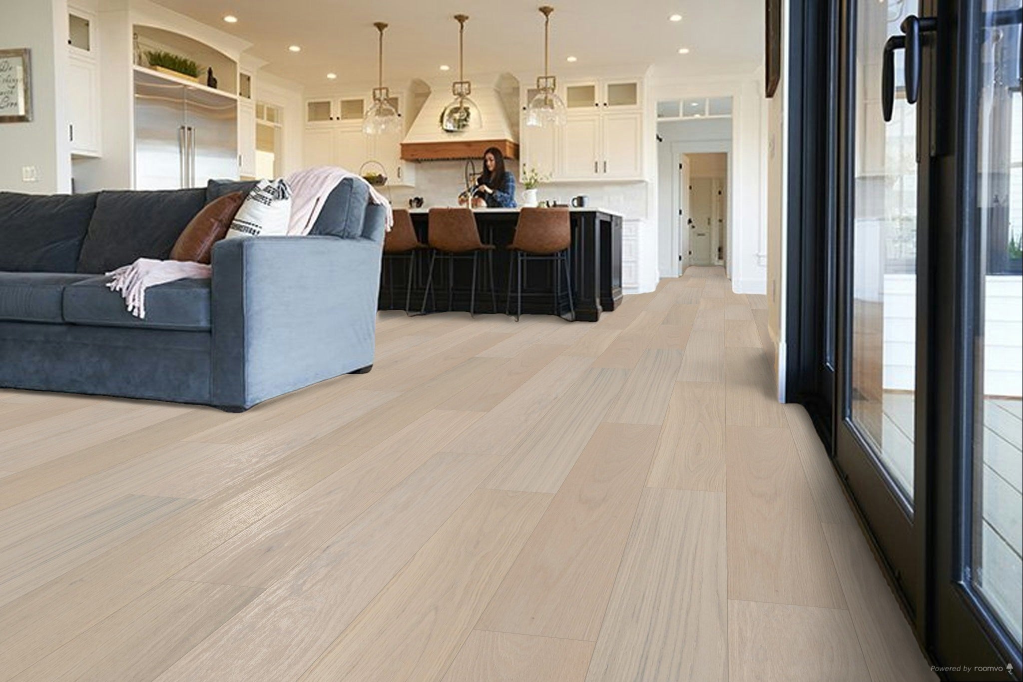 Light oak hardwood flooring in a modern, bright living room with a blue-gray sofa, kitchen island, and large glass sliding doors.